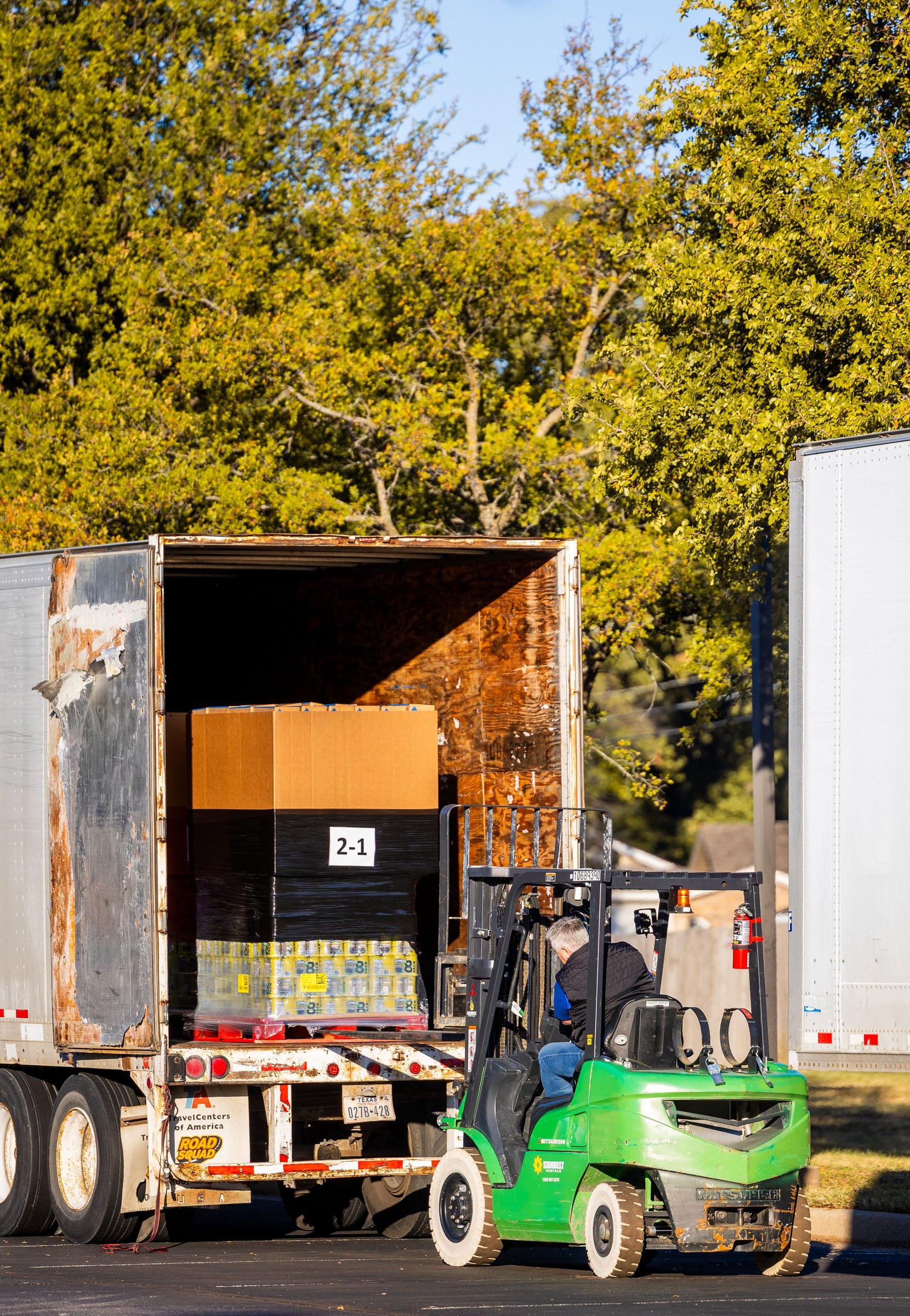 Forklift loading a pallet of goods into a truck in a tree lined outdoor work area